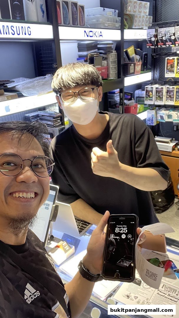 Two men smiling, one giving a thumbs up, in a phone repair shop with phone accessories on display.