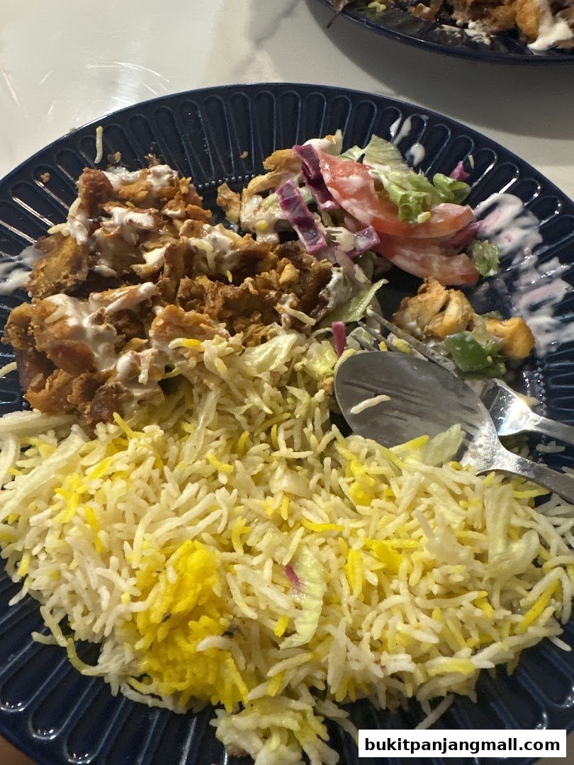 A plate of rice with chicken and salad, drizzled with sauce.