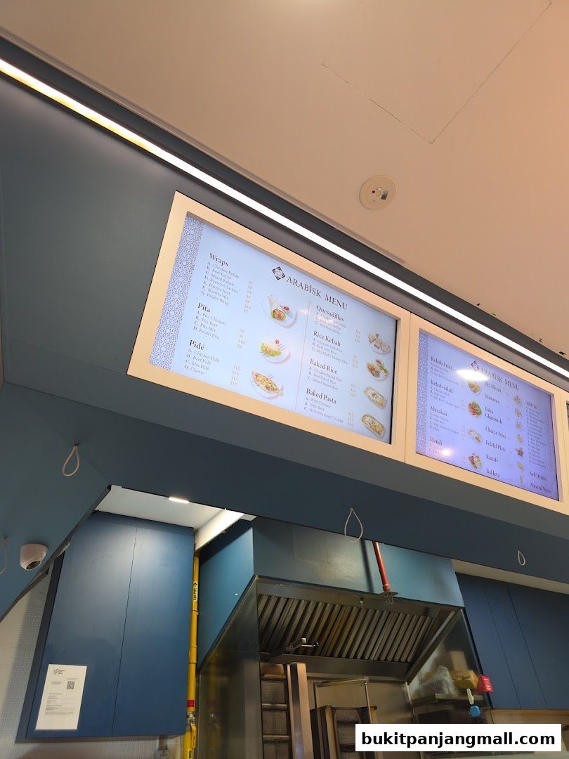 A digital menu board displaying various Arabic food items and prices.