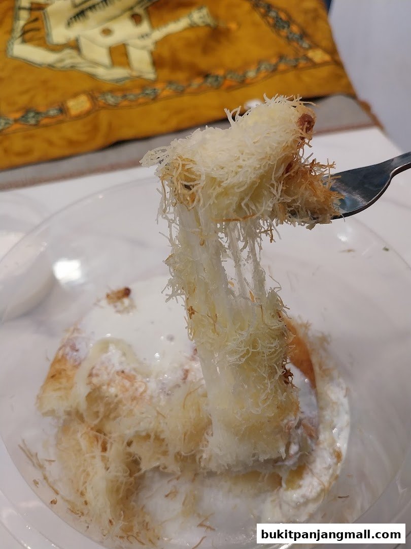 A fork lifts a piece of shredded pastry dessert covered in cream and syrup.