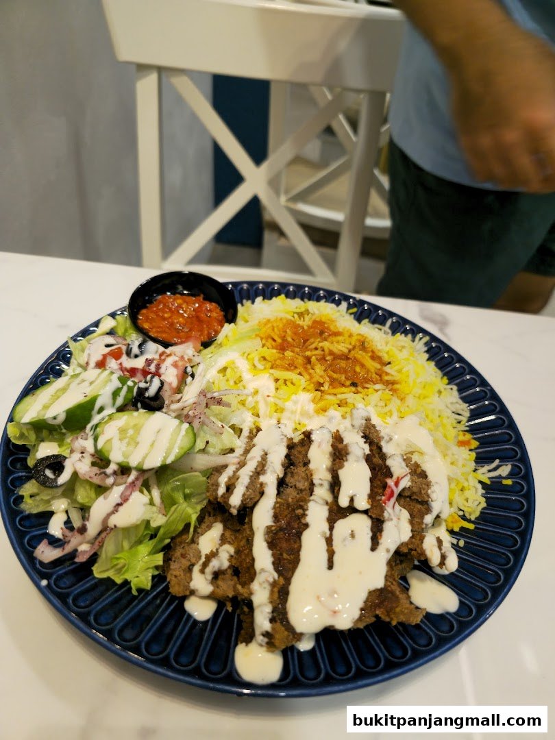 A plate of Middle Eastern food with rice, meat, salad, and sauce.