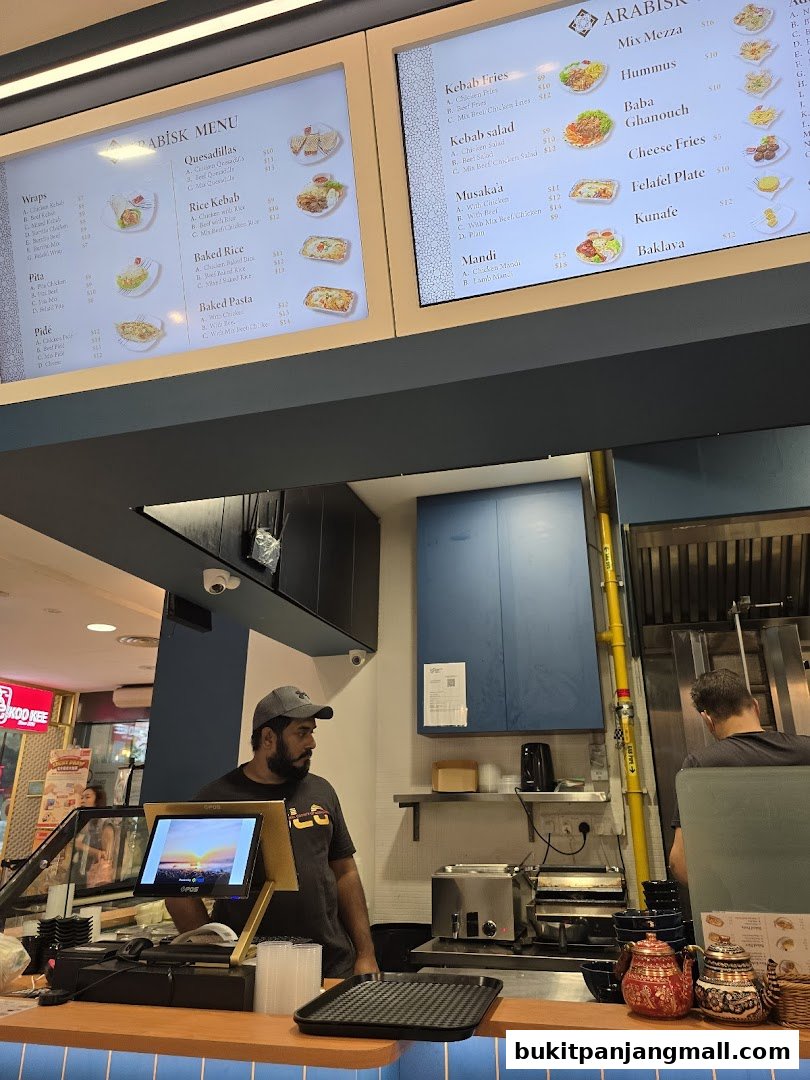 A digital menu board displaying various Arabic food items and prices.