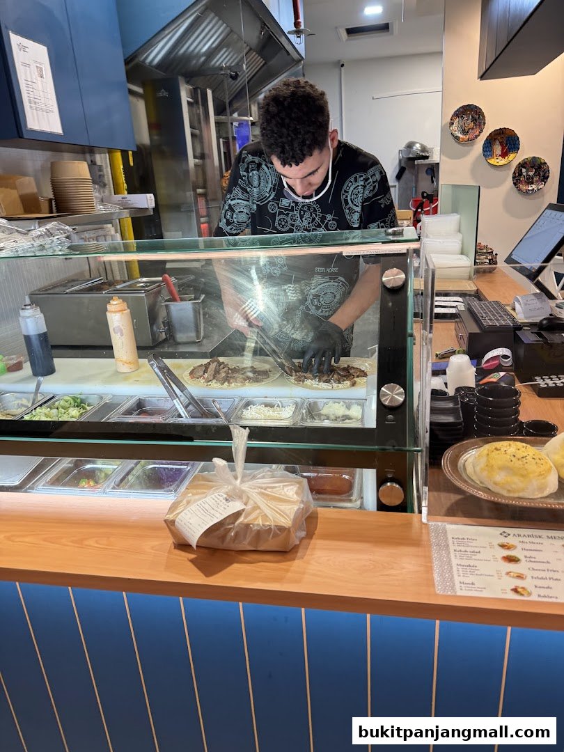 A chef prepares food behind a counter with fresh ingredients and a menu visible.