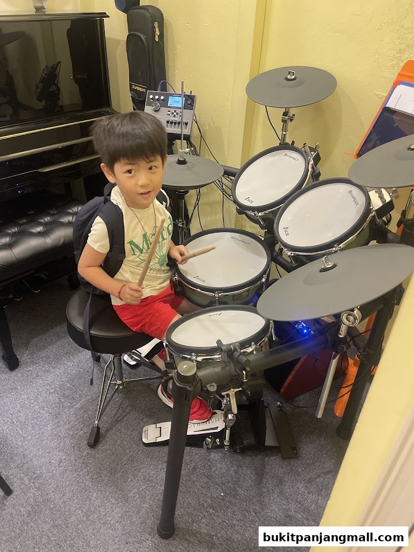A young boy sits at a drum set, holding drumsticks, in a music studio.
