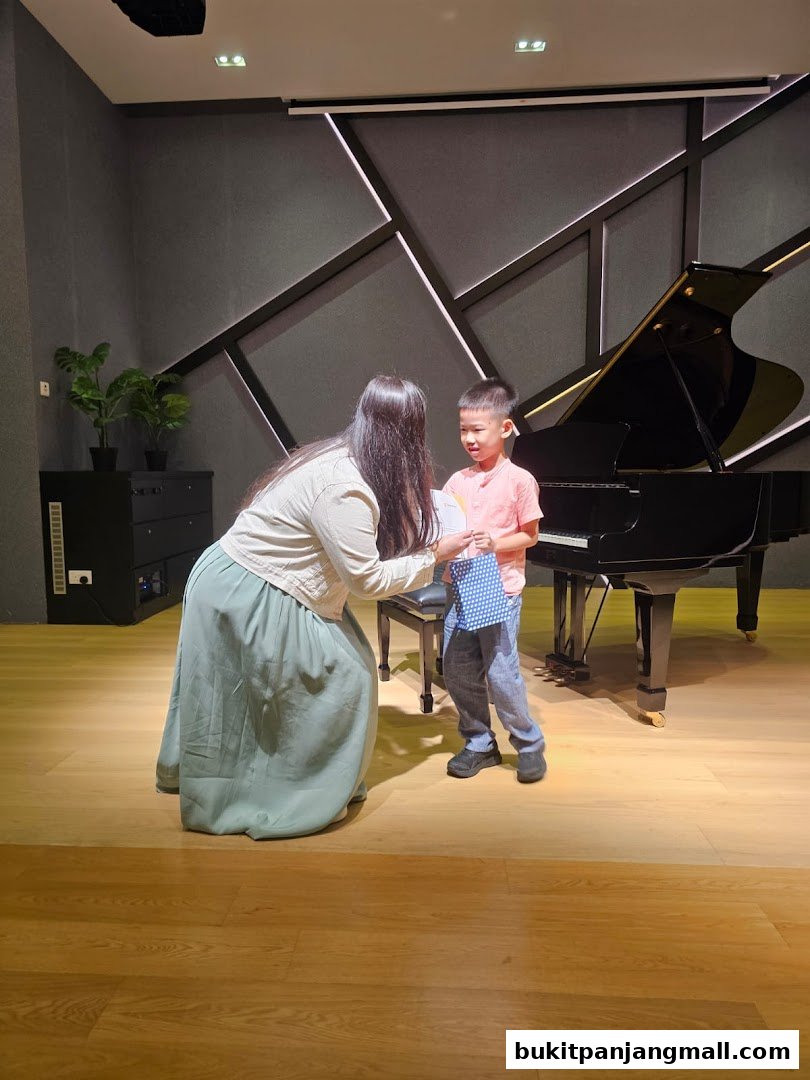 A teacher presents a certificate to a young student in front of a grand piano.