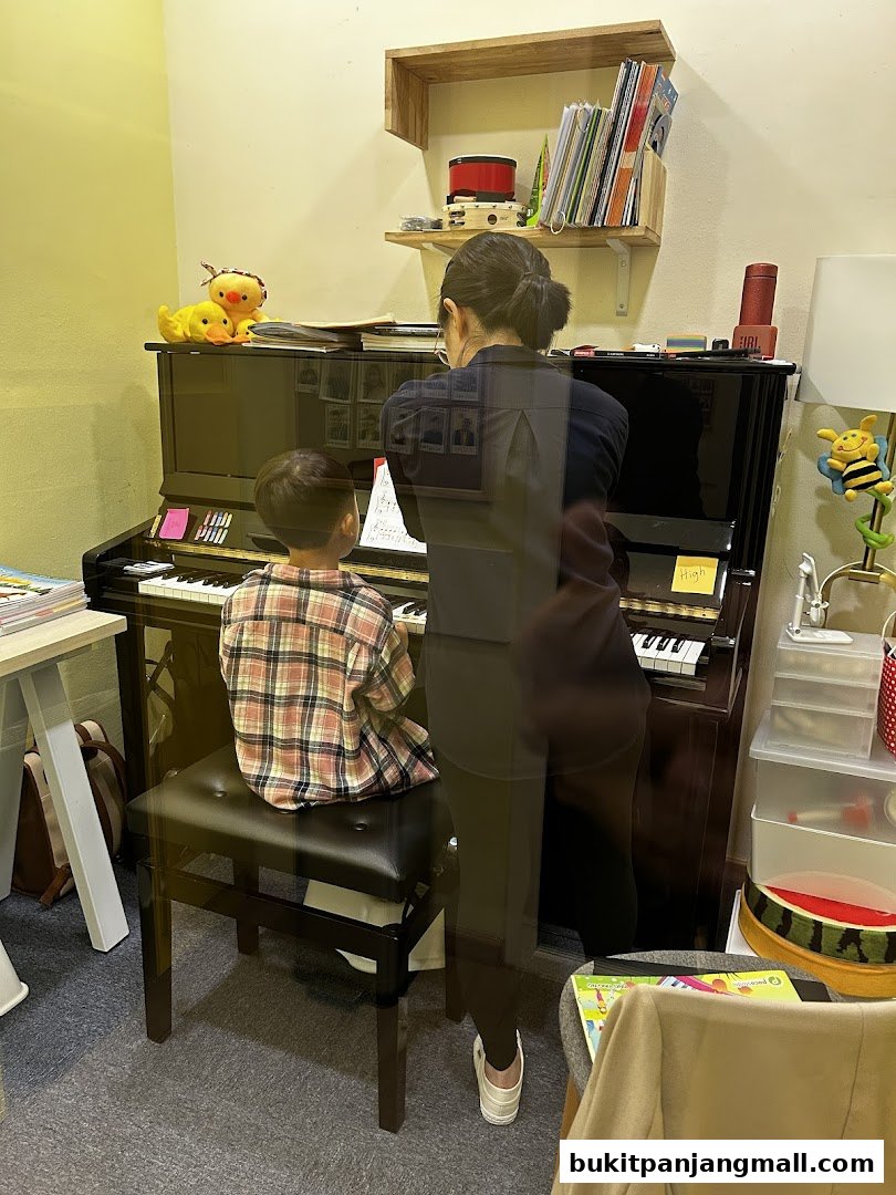 A teacher instructs a young student at a piano in a music classroom.
