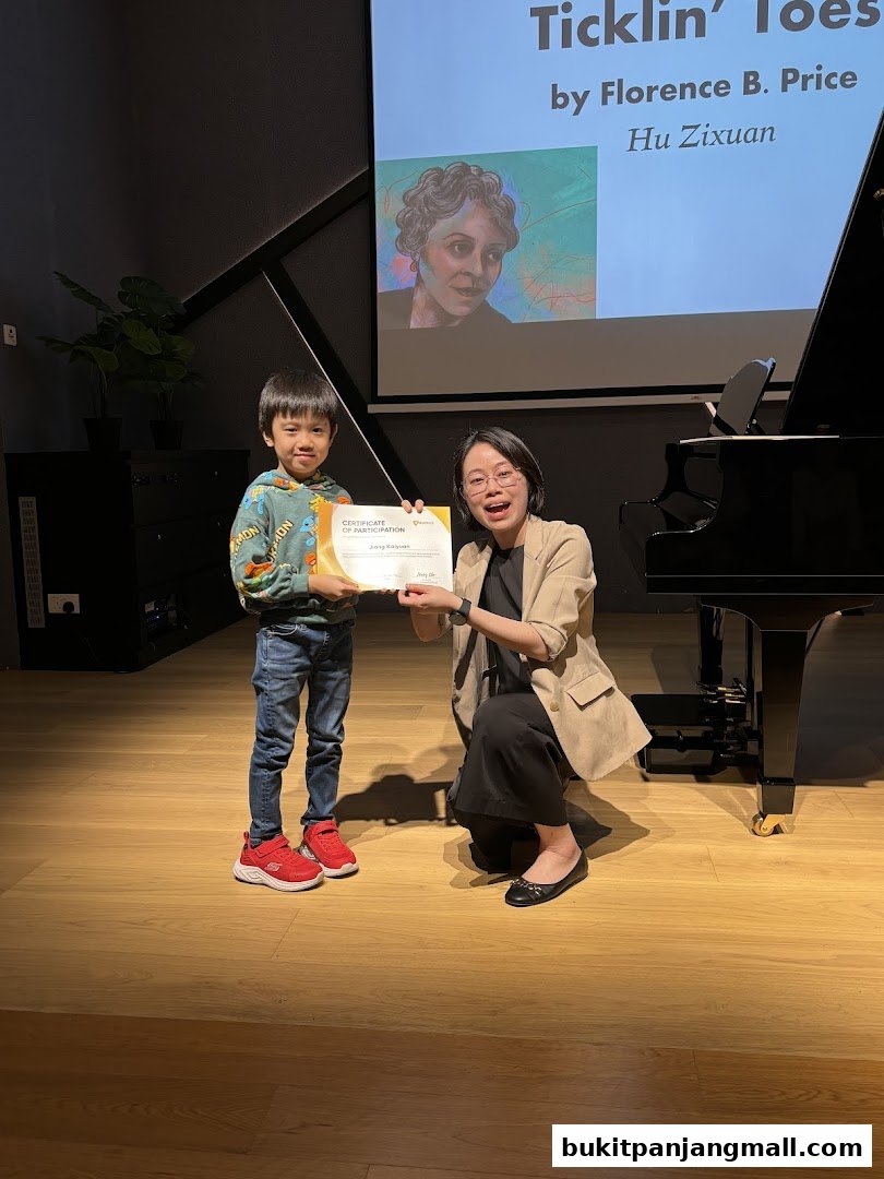 A child receives a certificate from an instructor in front of a piano and projector screen.