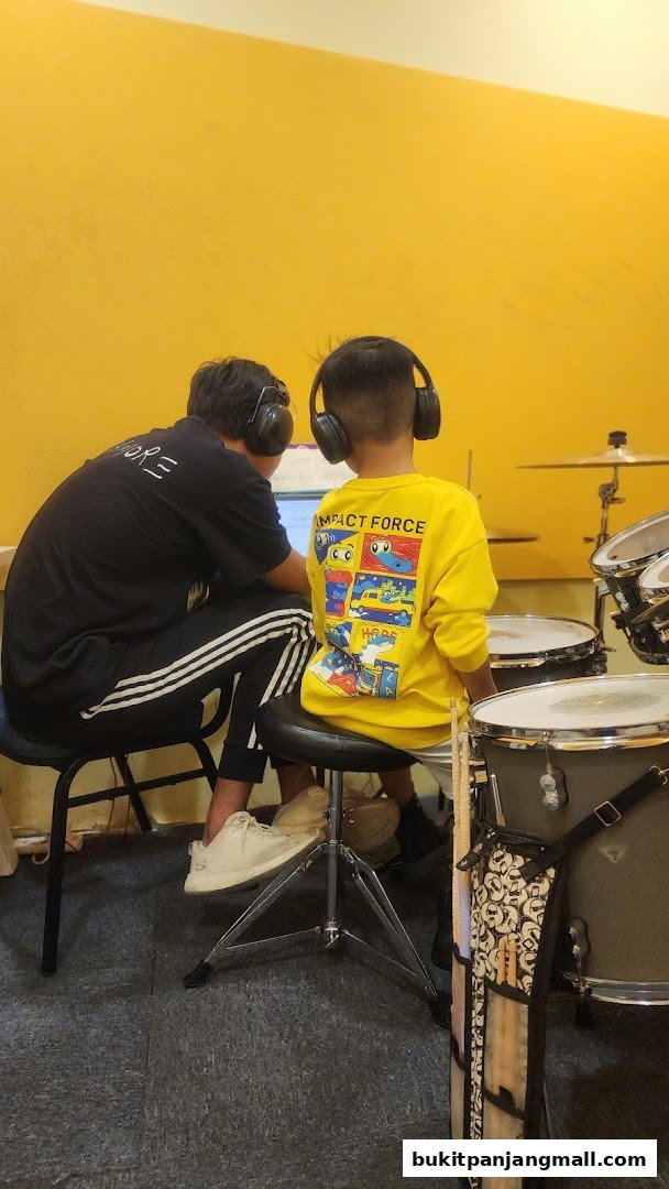 Two people wearing headphones are sitting in front of a drum set, possibly in a music lesson.