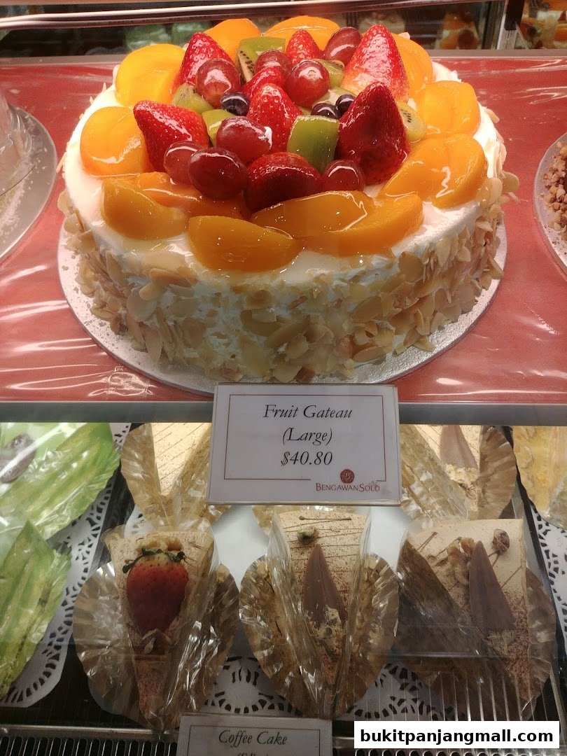 A large fruit gateau cake topped with fresh strawberries, grapes, peaches, and kiwi.