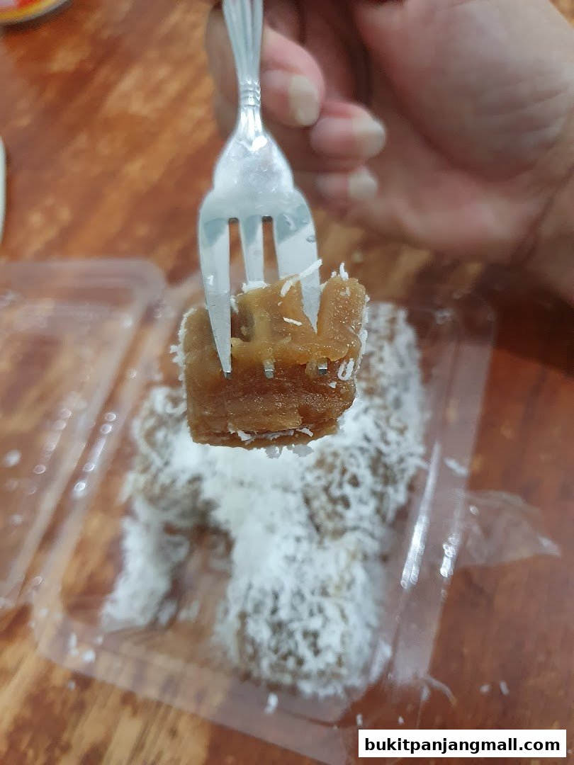 A fork is picking up a piece of traditional Indonesian sweet cake covered in shredded coconut.