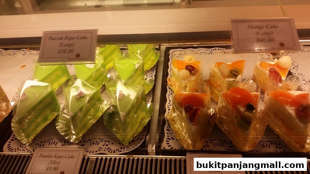 A display case filled with slices of Pandan Kaya Cake and Fruit Gateau.