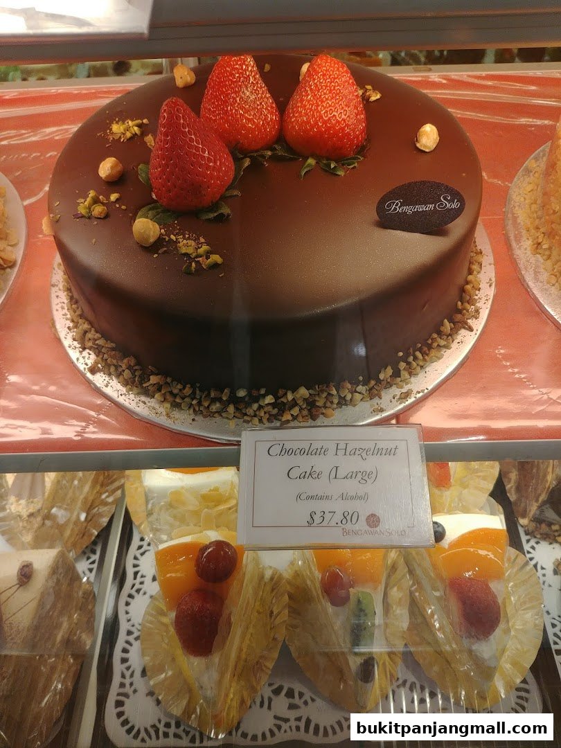 A large chocolate cake topped with strawberries and hazelnuts is displayed in a shop window.