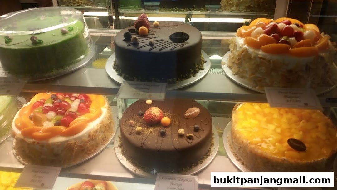 A display of various cakes, including chocolate, fruit, and green cakes, in a bakery.