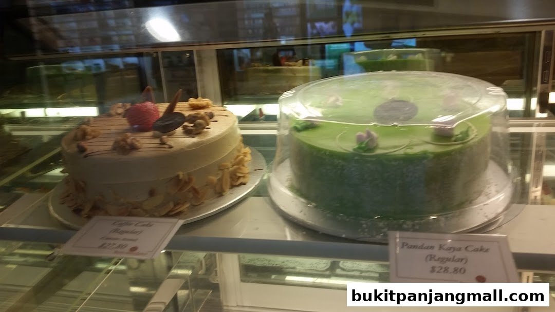 Two cakes, one coffee flavored and one green pandan kaya, displayed in a bakery case.