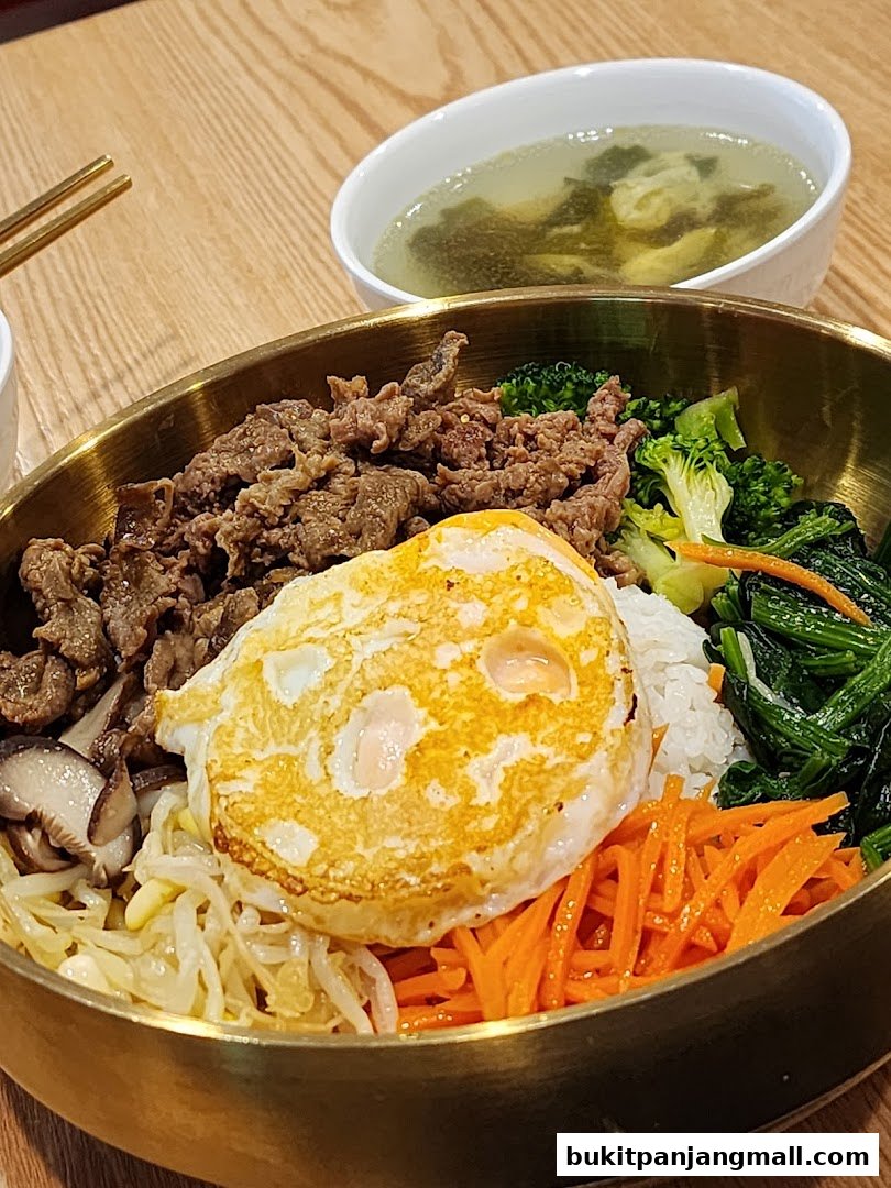 A close-up of a delicious bibimbap with beef, egg, vegetables, and a side of soup.