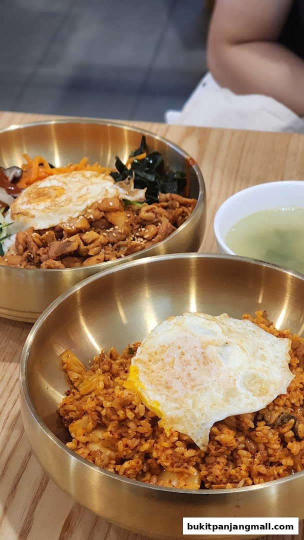Two bowls of Korean food, one bibimbap and one kimchi fried rice, topped with fried eggs.