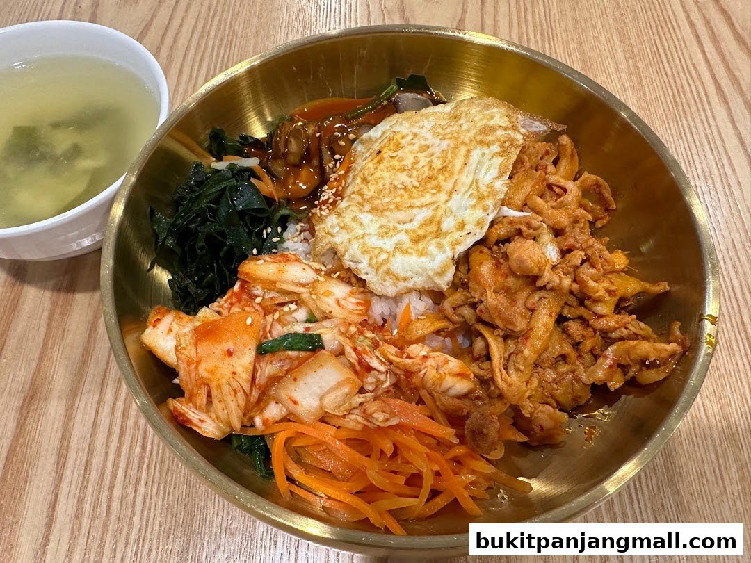 A delicious bowl of bibimbap with a fried egg, kimchi, and other toppings, served with a side of soup.