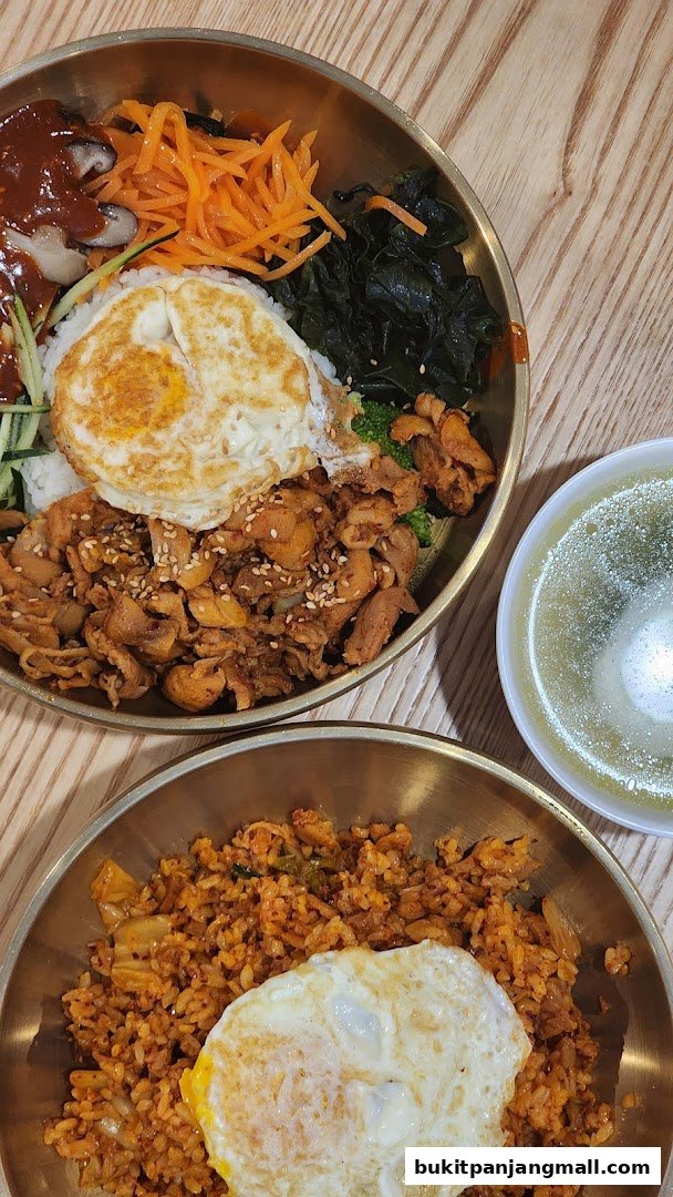Two bowls of Korean food, one bibimbap and one kimchi fried rice, with a side of soup.