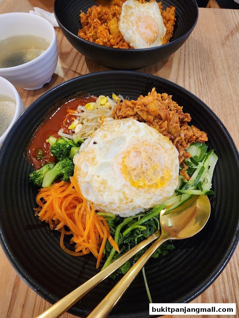Two bowls of Korean food, one bibimbap and one fried rice, with a side of soup.