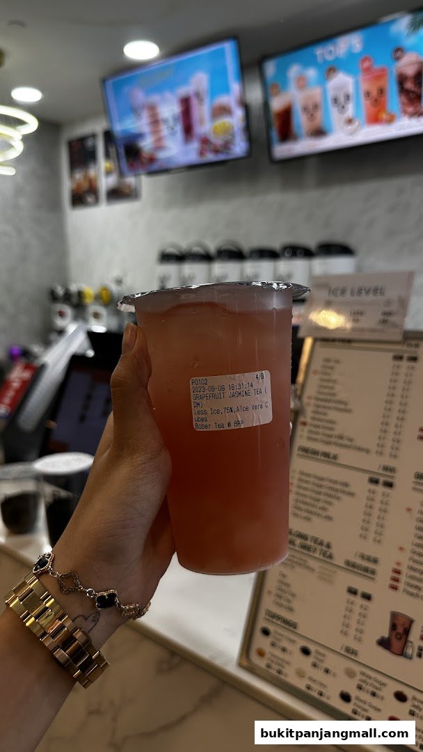 A hand holds a grapefruit jasmine tea with a label showing order details.
