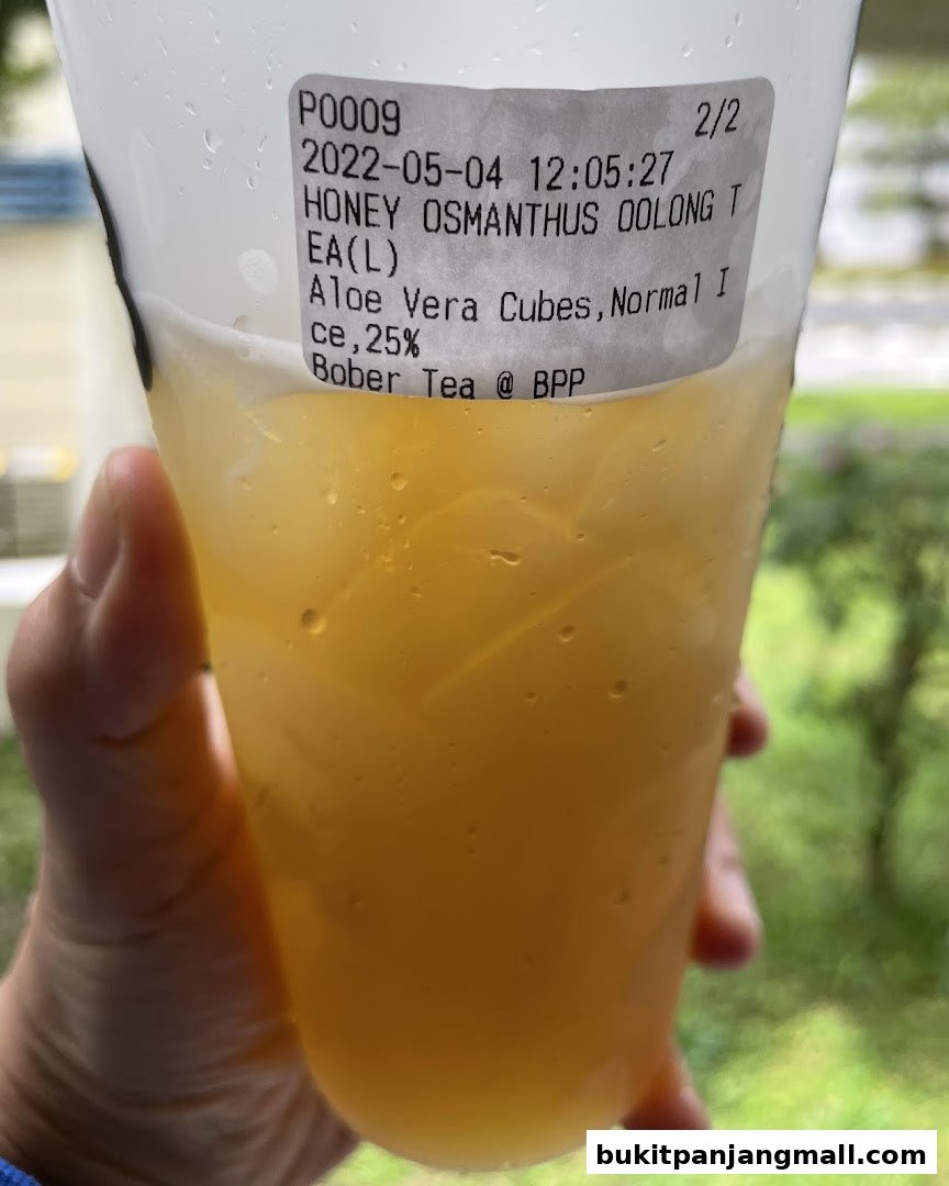 A hand holds a cup of Honey Osmanthus Oolong tea with aloe vera cubes.