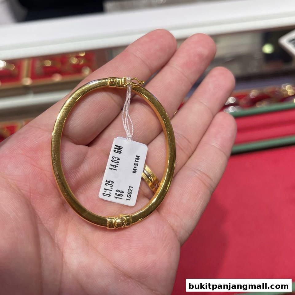 A hand holds a gold bracelet with a price tag showing weight and code.