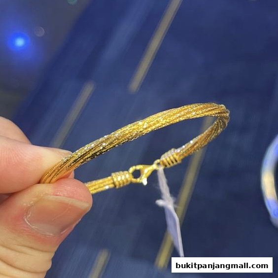 A hand holds a sparkling gold bracelet with a textured finish and a clasp.