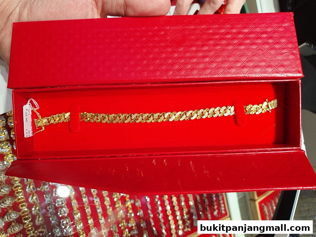 A gold bracelet displayed in a red jewelry box, with other jewelry visible in the background.