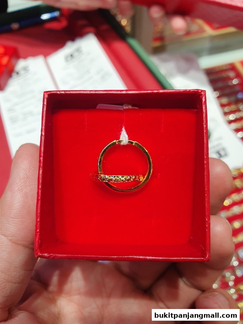 A hand holds a red box containing a gold ring with a textured band.