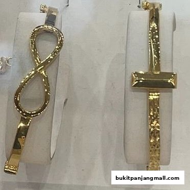 Two gold bracelets, one with an infinity symbol and the other with a cross design, displayed on white stands.