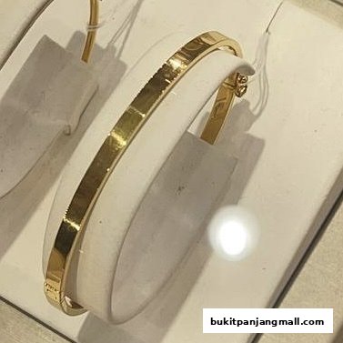A close-up of a gold bracelet displayed on a white stand in a jewelry store.
