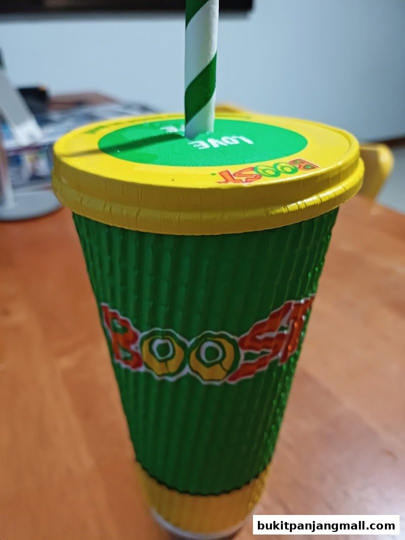 A green Boost Juice cup with a yellow lid and a striped straw.