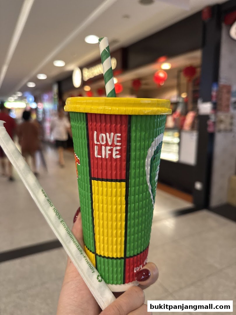 A hand holds a colorful Boost Juice cup with a striped straw and eco-friendly packaging.
