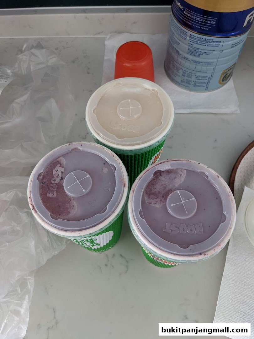 Three Boost Juice drinks are arranged on a counter with a can of formula and a plastic bag.