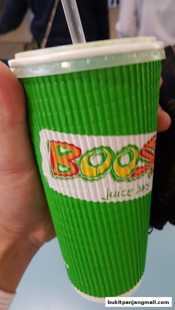 A hand holds a green corrugated cup with the Boost Juice logo and a straw.