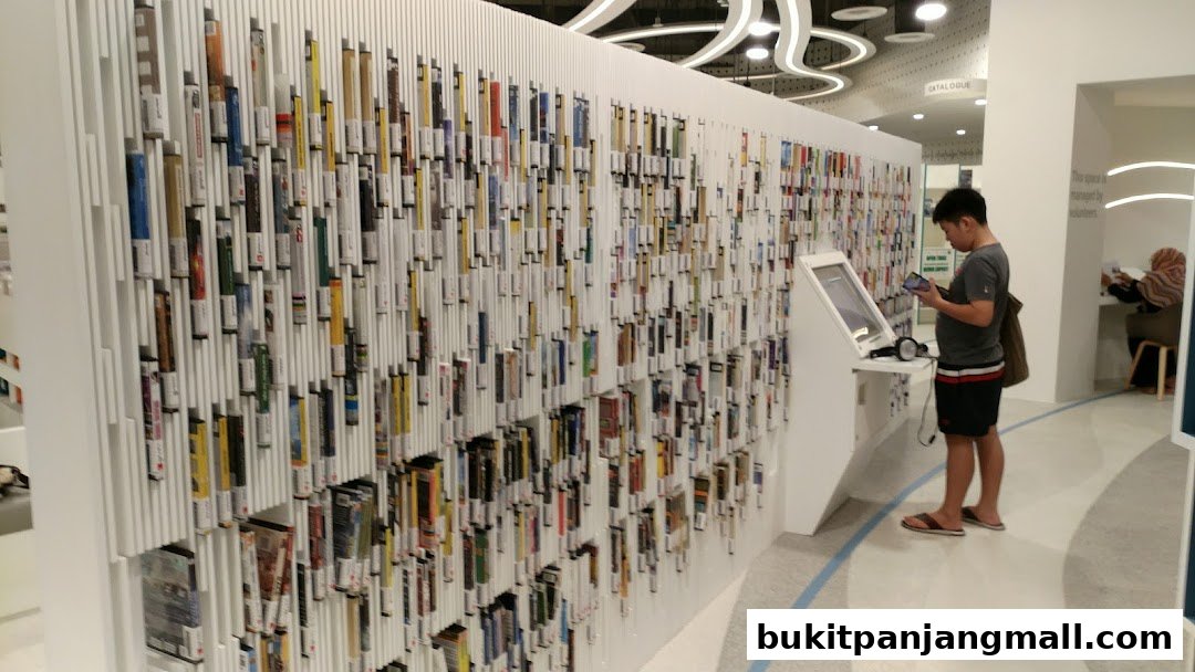 A young man uses a digital kiosk in a modern library with extensive book displays.