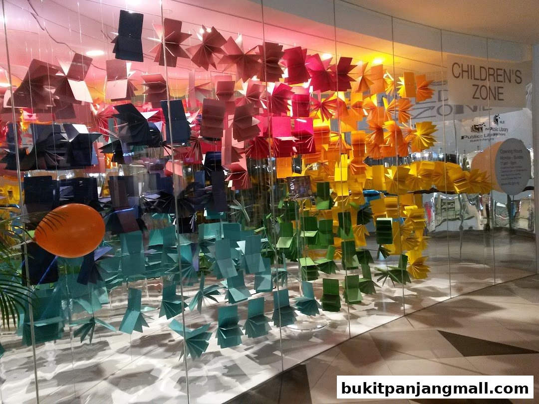 A colorful display of origami decorations hangs in front of a glass window, with a sign for the Children's Zone visible.