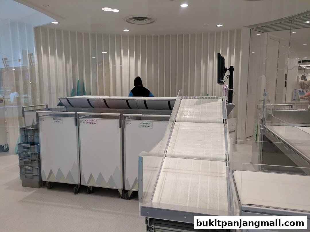 A person in a hoodie stands behind a counter with sorting bins labeled with days of the week.
