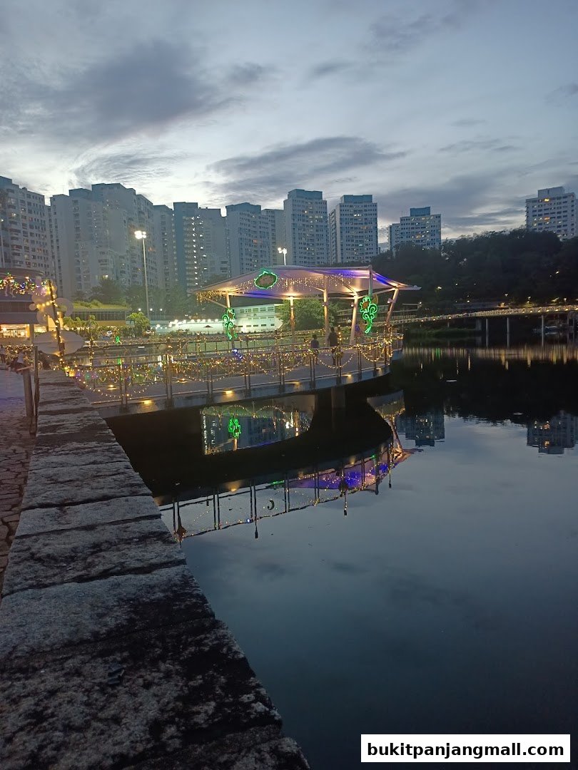 A scenic view of a waterfront pavilion decorated with lights at dusk, with apartment buildings in the background.