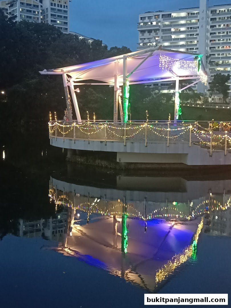 A covered pavilion with decorative lights reflected in the water at dusk.