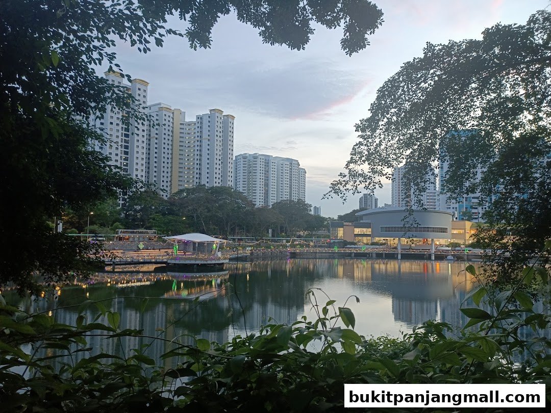 A serene lake reflects buildings and a stage with lights at dusk.
