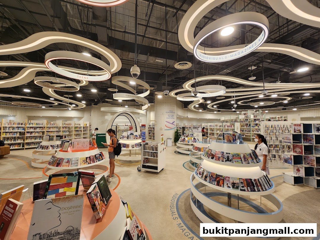 Interior of a modern library with bookshelves, display stands, and people browsing.