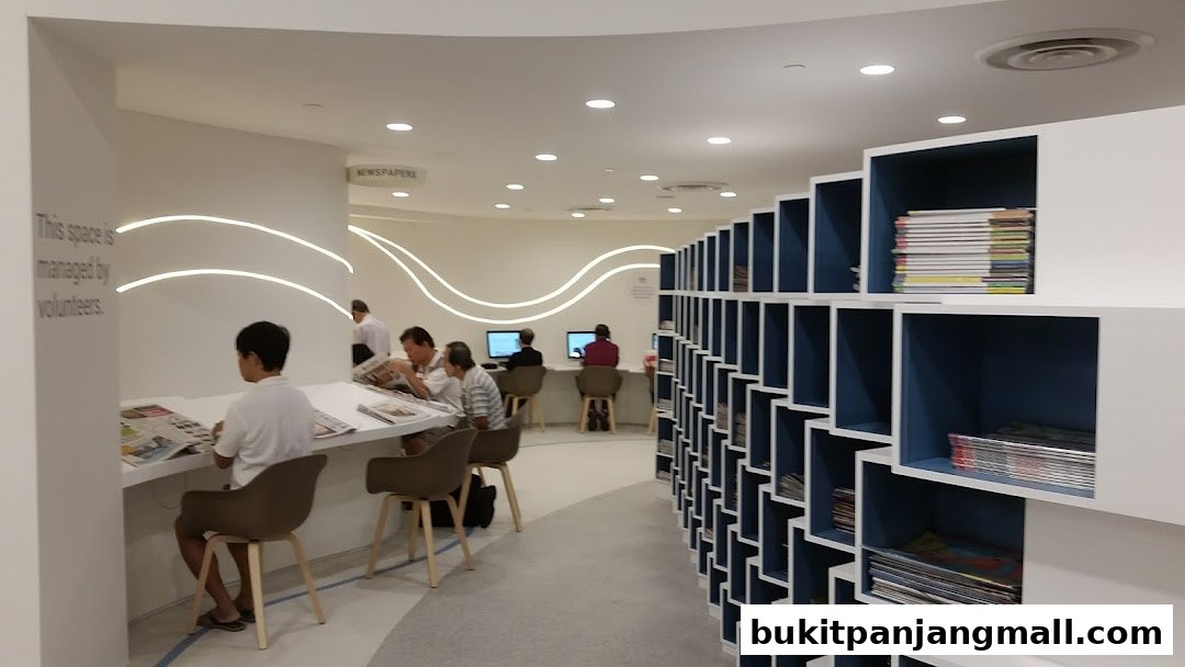 People reading newspapers and using computers in a modern library with bookshelves.