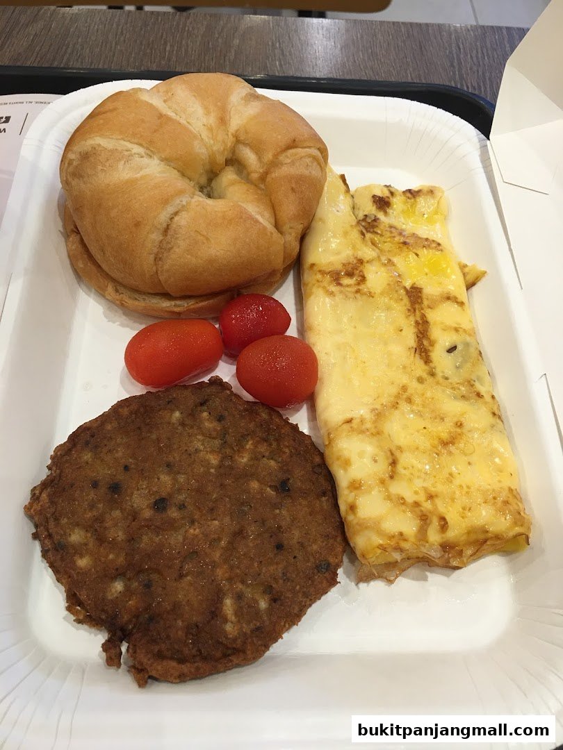 A breakfast meal with a croissant, omelet, sausage patty, and cherry tomatoes.