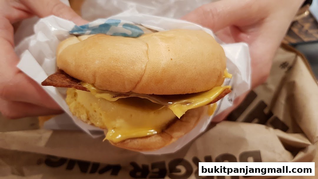 A close-up of a person holding a Burger King breakfast sandwich with bacon and cheese.