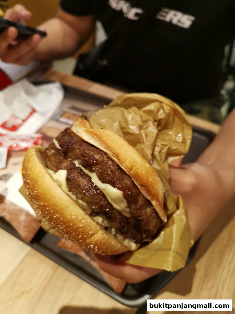 A person holds a double-patty burger wrapped in paper, ready to eat.