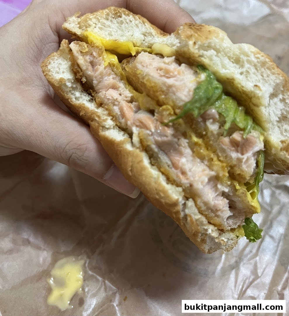 A hand holds a salmon burger with lettuce and sauce on a bun.