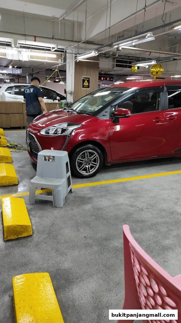 A red car is being serviced by a crew member in a workshop.
