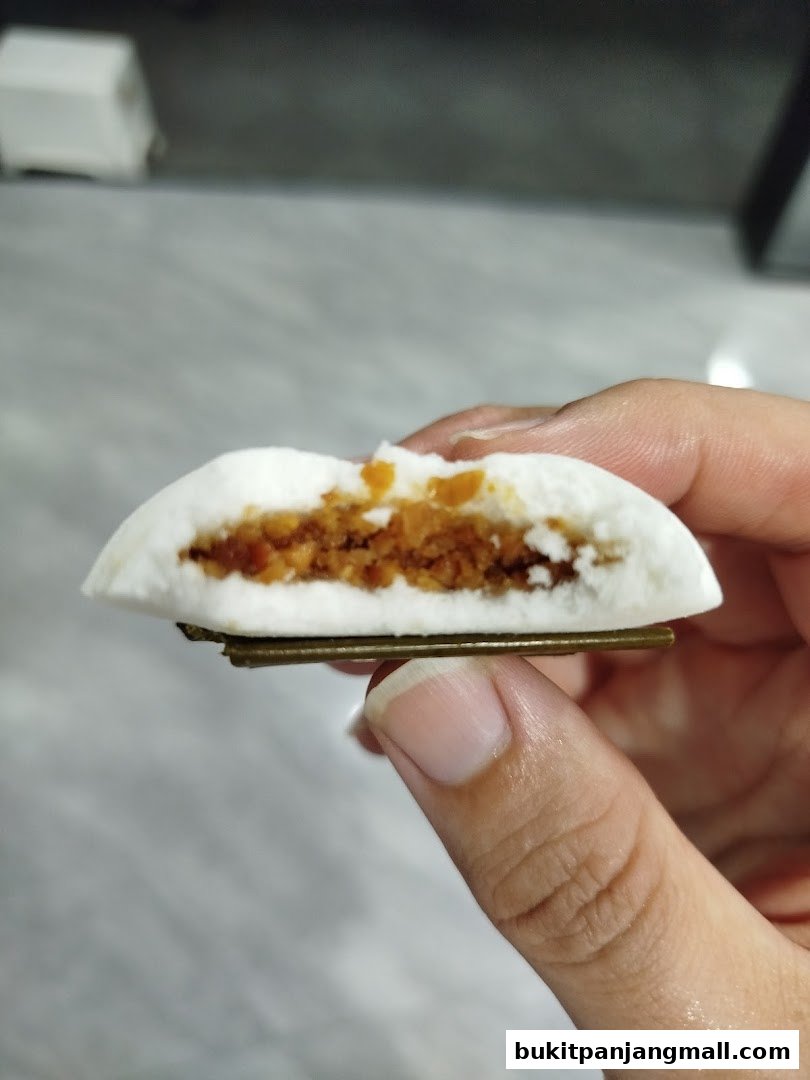 A hand holds a sliced Tutu Kueh with a sweet, crumbly filling.