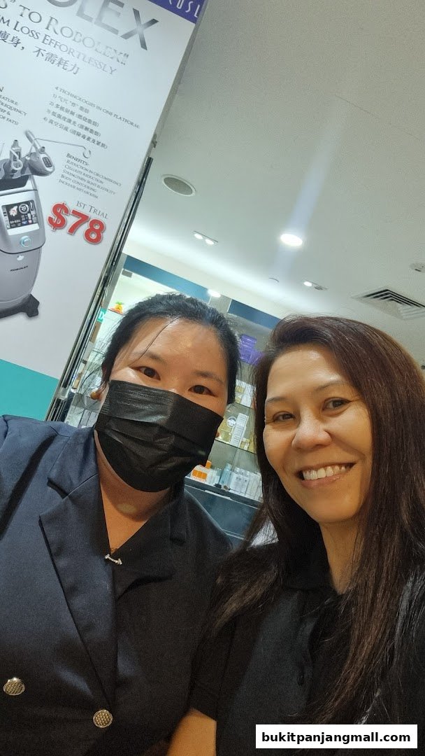 Two women smiling at the camera in front of a beauty spa advertisement.